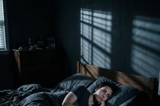 A realistic photo having sleep paralysis explained: a woman waking up in a dark room unable to move.