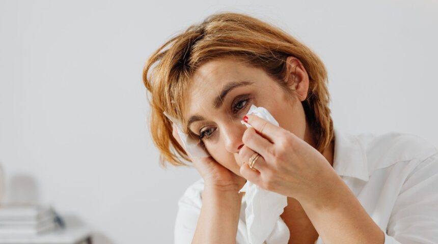 Woman holding back tears with a tissue while experiencing a lump in her throat before crying